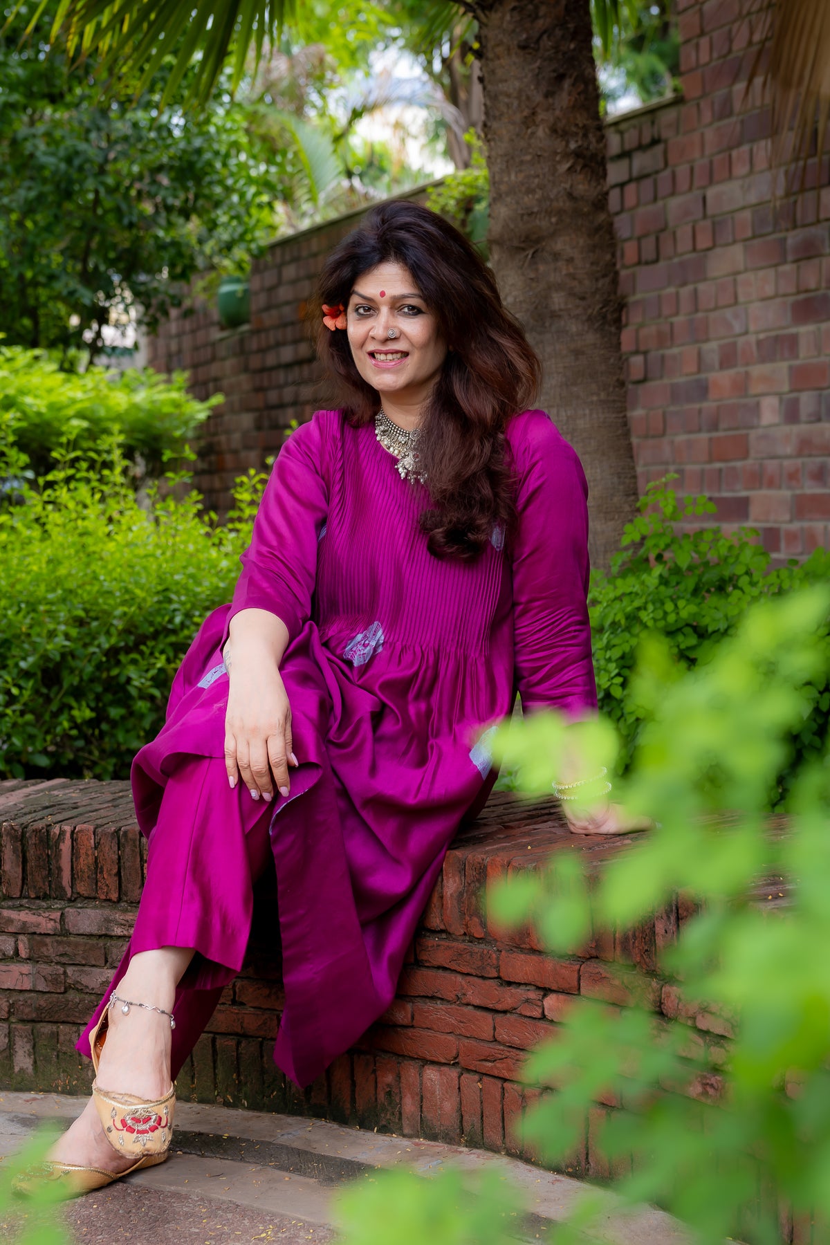 front view of model sitting in preet bandhej magenta kurta set.